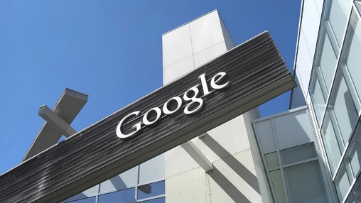 Google branded sign mounted on a dark angular structure outside a modern office building under blue sky