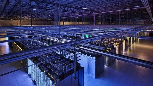 Wide-angle view of a large data centre with illuminated server rows and an industrial steel ceiling structure