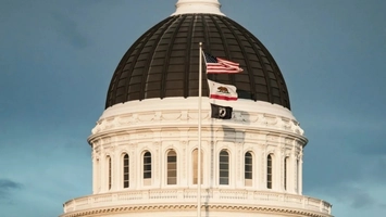 Close-up of a white neoclassical government building dome with flags on a central mast under an overcast sky