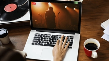 Person watching a live streamed music concert on a laptop with a vinyl record and coffee cup on the desk